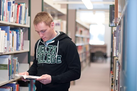 Student looking at books in Library rows