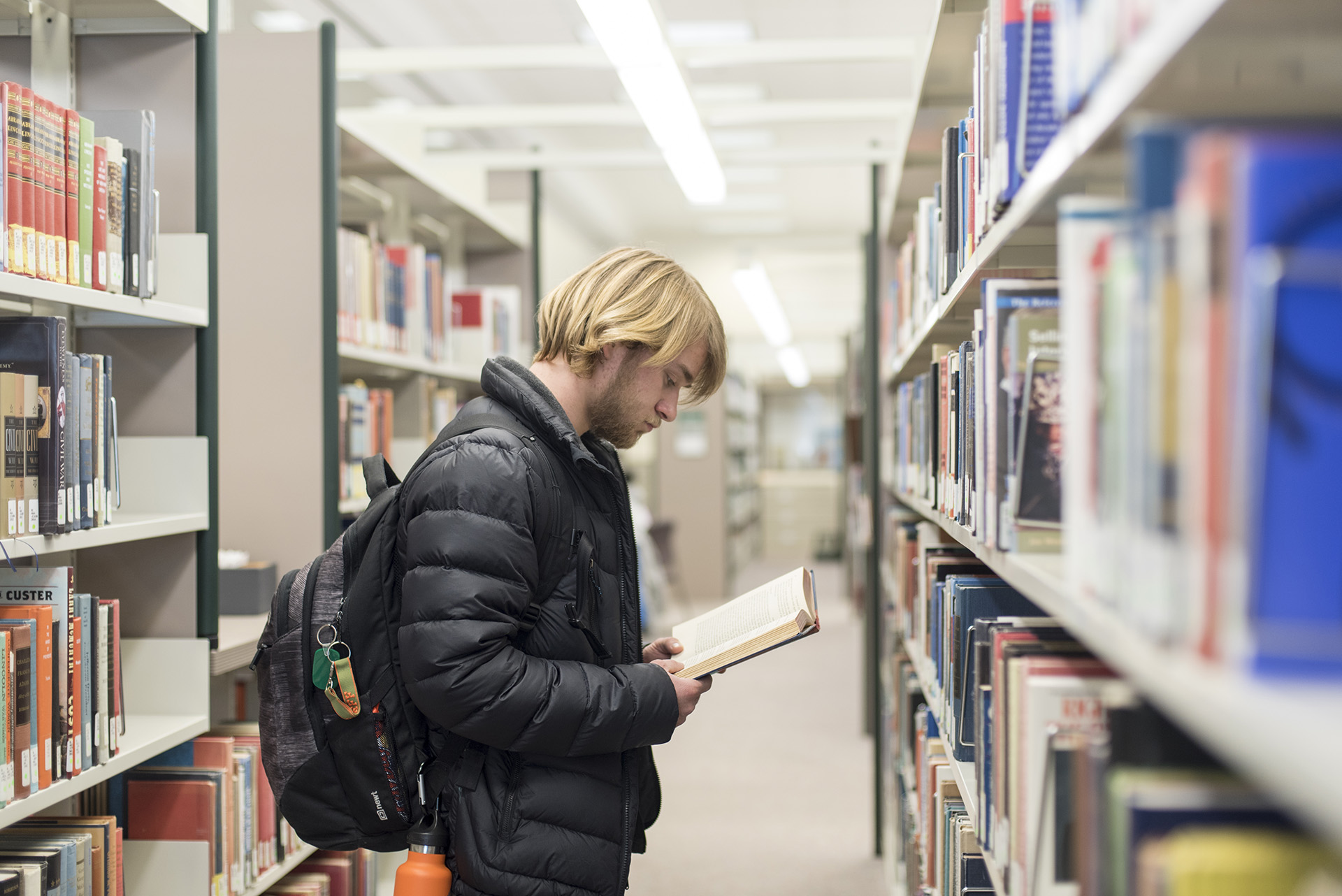 Student looking at books in Library rows.